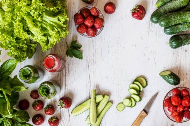 Üstten Görünüm. Taze yeşil smoothies ve hafif ahşap arka plan üzerinde malzemelerle çilek güler yüzlü. Sağlıklı Detoks içecekler.