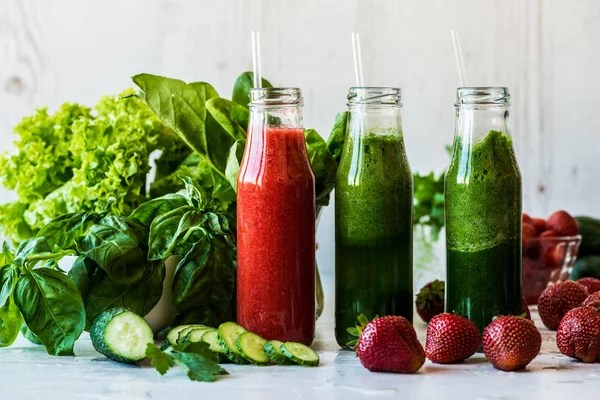 Taze yeşil smoothies ve hafif ahşap arka plan üzerinde malzemelerle çilek güler yüzlü. Sağlıklı Detoks içecekler.