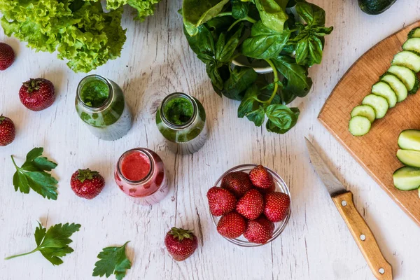 Üstten Görünüm. Taze yeşil smoothies ve hafif ahşap arka plan üzerinde malzemelerle çilek güler yüzlü. Sağlıklı Detoks içecekler.