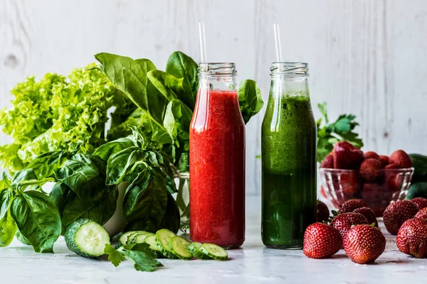 Yeşil smoothie ve çilek smoothie malzemeler hafif ahşap zemin ile iki küçük şişelerde. Sağlıklı Detoks içecekler.
