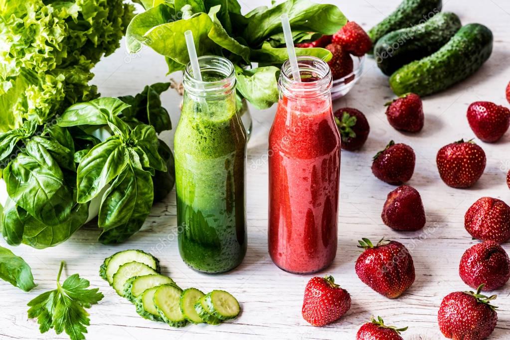 Green smoothie and strawberry smoothie in two small bottles with ingredients on a light wooden background. Healthy detox drinks.