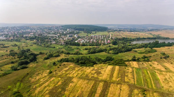 Вид с воздуха на летнюю сельскую местность. Полет над зеленым полем и городом — стоковое фото