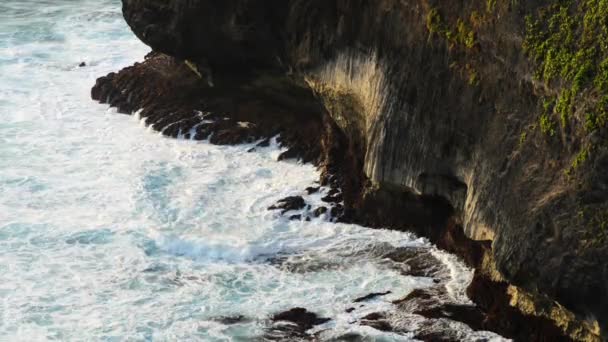 Волны, ударяющиеся о скалы на тропическом пляже, образуют всплеск формы. Мощные волны на скалистом пляже. Известный храм Улувату в Бали, Индонезия . — стоковое видео