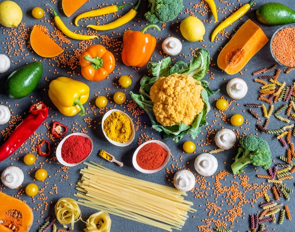 Diverse verdure fresche colorate, spaghetti e fettuccine, spezie. ingredienti vegani crudi sani per cucinare su fondo grigio. Posa piatta, vista dall'alto . — Foto Stock