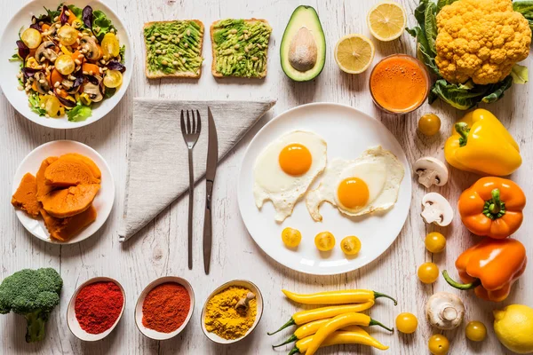 Cibo sano per la colazione. Uova fritte, panini vegani all'avocado, insalata di verdure, zucca bollita, succo fresco di carota e diverse verdure e spezie biologiche colorate — Foto Stock