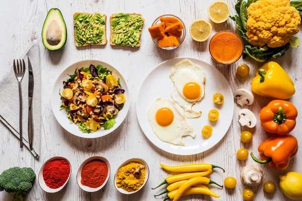 Cibo sano per la colazione. Uova fritte, panini vegani all'avocado, insalata di verdure, zucca bollita, succo fresco di carota e diverse verdure e spezie biologiche colorate — Foto Stock