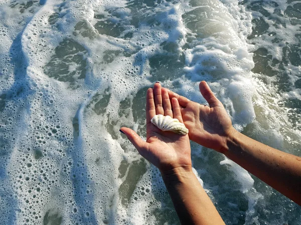 Des mains féminines tenant un coquillage au-dessus des vagues. Gros plan . — Photo