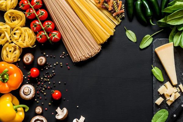 Verschillende verse ingrediënten voor het koken Italiaanse pasta, spaghetti, fettuccine, fusilli en groenten op een zwarte achtergrond met presentexemplaar ruimte. Plat lag, top uitzicht. — Stockfoto