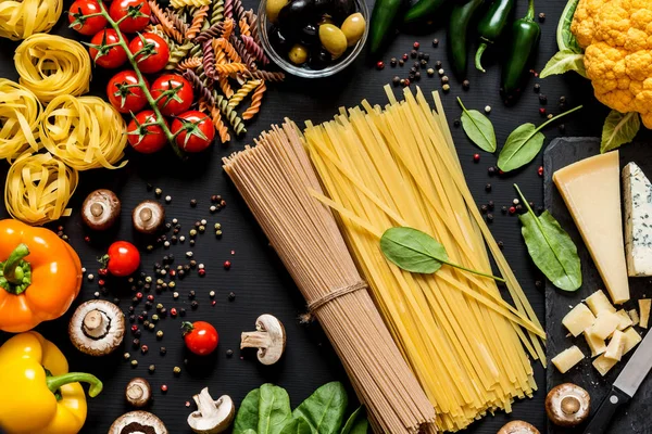 Verschillende verse ingrediënten voor het koken Italiaanse pasta, spaghetti, fettuccine, fusilli en groenten op een zwarte achtergrond. Plat lag, top uitzicht. — Stockfoto