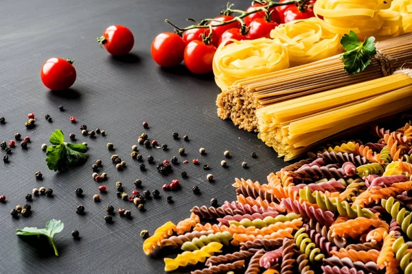 Divers soort de Italiaanse rauwe Pasta. kleurrijke fusilli pasta, spaghetti, fettuccine met tomaten op een zwarte achtergrond. Closeup — Stockfoto