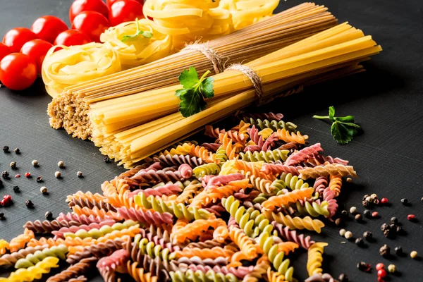 İtalyan pişmemiş makarna çeşitli tür. renkli düdük makarna, spagetti, fettuccine domates siyah bir arka plan ile. Portre