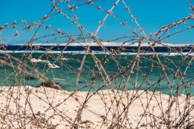 Eski deniz infront tel dikenli. Tel ve mavi gökyüzü bulutlu. Güvenlik çit dikenli tel mavi gökyüzü ve denizin karşı. Yakın çekim.