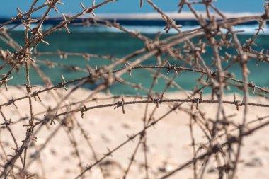 Eski deniz infront tel dikenli. Tel ve mavi gökyüzü bulutlu. Güvenlik çit dikenli tel mavi gökyüzü ve denizin karşı. Yakın çekim.