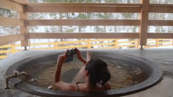 Uma menina está tomando banho e fazendo uma selfie na cuba de ferro fundido com água mineral . — Vídeo de Stock