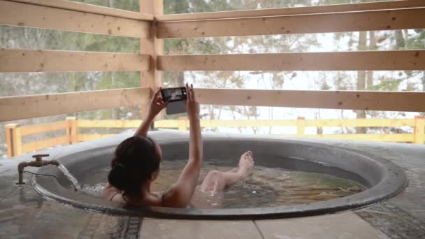 Una chica se está bañando y haciendo una selfie en la tina de hierro fundido con agua mineral . — Vídeos de Stock