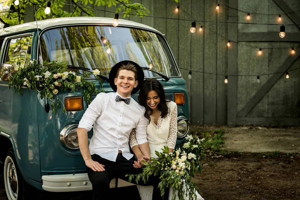 Cheerful happy young couple sit on the bumper retro-minibus.