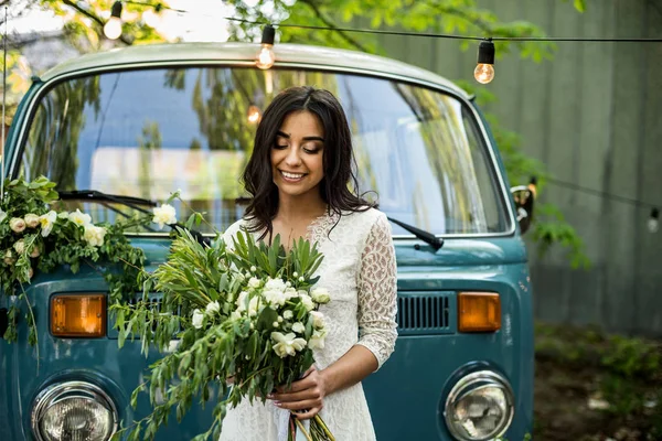 Glada lyckliga unga bruden hålla bukett nära retro-minibuss. Närbild. — Stockfoto