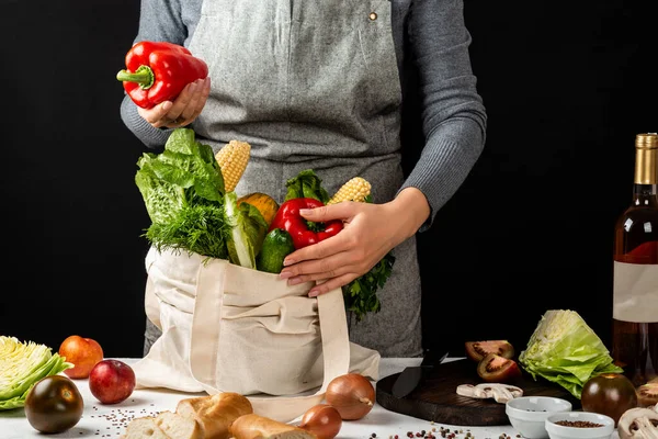 Woman holds an cotton eco bag full of different fresh vegetables and red pepper in hand. Cooking healthy clean food. Zero waste purchases concept.