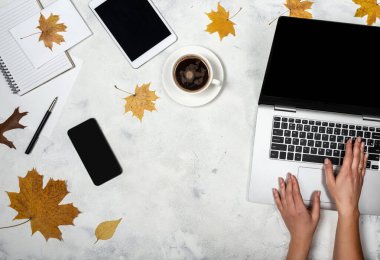 Dizüstü bilgisayarı, sonbahar yaprakları, bir fincan kahve, tablet, akıllı telefon, not defteri olan çalışma alanı. Sonbahar Serbest İşyeri 'nin en üst görünümü.