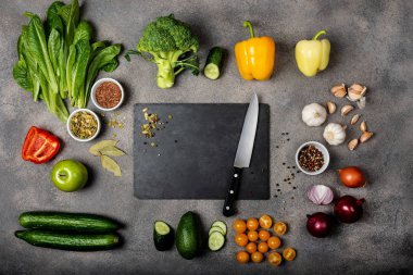 Sağlıklı bir yemek hazırlamak için gerekli malzemeler. Farklı sebzeler, baharatlar ve gri arka planda bıçak olan bir kara tahta. Diyet konsepti. Metin için boşluk olan üst görünüm.