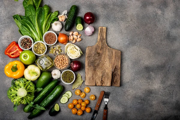 Skład ze składnikami do przygotowania zdrowej żywności wegetariańskiej. Różne warzywa i przyprawy oraz drewniana deska na szarym tle. Koncepcja diety. Widok z góry — Zdjęcie stockowe