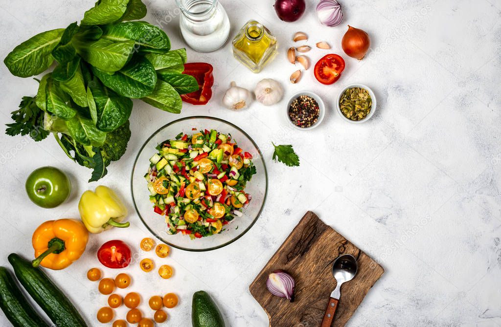 Homemade salad from various organic vegetables in a glass bowl with ingredients and spices on white background. Top view. Healthy diet food concept