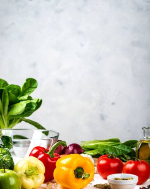 Masanın üzerinde çok renkli biber, çeşitli sebze ve baharatlar var. Pişirme salatası için gerekli malzemeler hafif bir arka planda, mesaj için de yer var. Sağlıklı diyet vegan gıda konsepti.