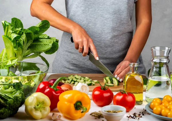 Una donna taglia il cetriolo, cucinando un'insalata in cucina. Dieta sana concetto . — Foto Stock