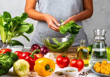 Kadın yeşil marul salatası hazırlıyor, mutfakta cam kasede salata pişiriyor. Sağlıklı diyet kavramı.