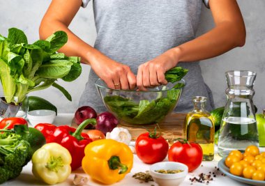 Kadın yeşil marul salatası hazırlıyor, mutfakta cam kasede salata pişiriyor. Sağlıklı diyet kavramı.