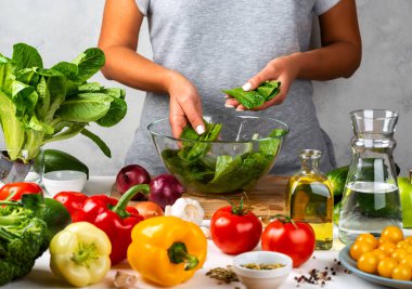 Kadın yeşil marul salatası hazırlıyor, mutfakta cam kasede salata pişiriyor. Sağlıklı diyet kavramı.