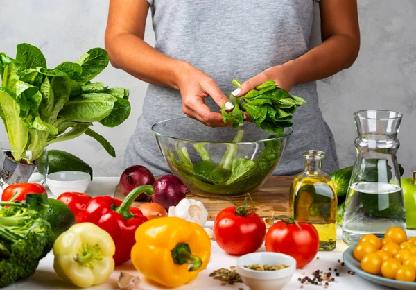 Kadın yeşil marul salatası hazırlıyor, mutfakta cam kasede salata pişiriyor. Sağlıklı diyet kavramı.