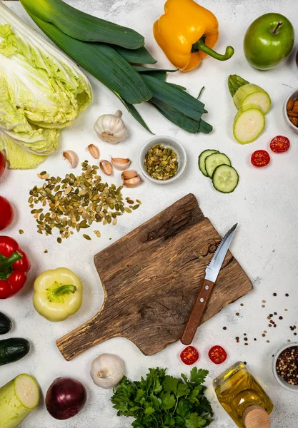 Houten plank met mes en verschillende groenten op een lichte ondergrond. Bovenaanzicht. — Stockfoto