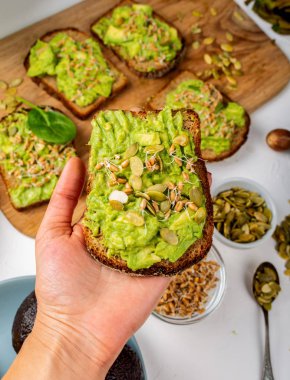 Avokado Guacamole Sandviçi, balkabağı tohumları ve buğday tohumlarıyla dolu bir kadın elinde.