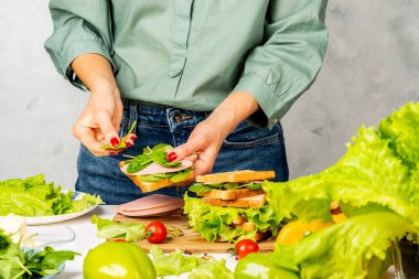 Kadın jambon, tereyağı, marul ve ıspanaktan sandviç yapıyor.