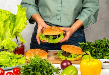 Kadın mutfakta elinde bir hamburger tutuyor.