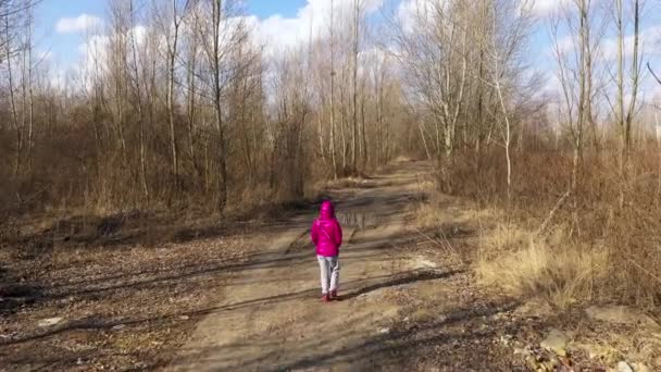 Dívka v teplákové soupravě a zářivě teplé bundě kráčí lesem — Stock video