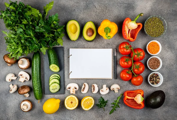 Different vegetables and ingredients for cooking delicious dishes. A book for writing recipes lies on a table surrounded by food. Copy space for text — ストック写真