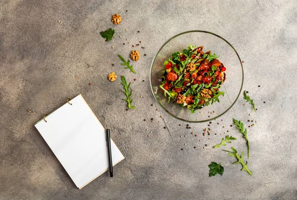 Plantaardige salade met arugula, tomaten, avocado, besprenkeld met balsamico saus. Een boek voor het schrijven van recepten ligt op tafel. Kopieer ruimte voor tekst — Stockfoto