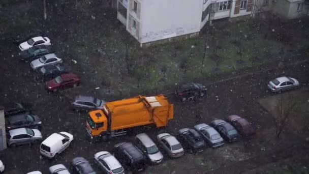 Un camión de basura conduce al patio para recoger los contenedores de basura. Tormenta de nieve en la ciudad en primavera — Vídeos de Stock