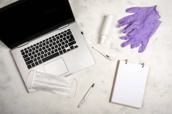 Online work and education in conditions of quarantine. Stay at home. Laptop, notebook, pen, surgical mask, hand sanitizer and digital thermometer on the white background. Concept of the fight against coronovirus, covid-19. Social isolating. Flat lay.