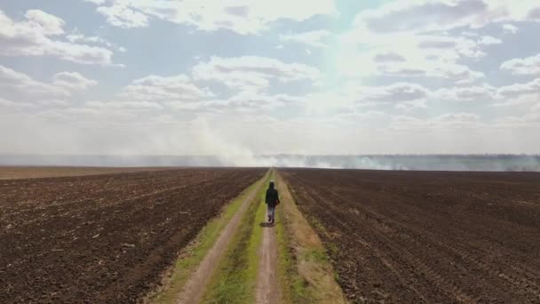 A girl walks along the road in the field to the place where there is a fire — Stock Video