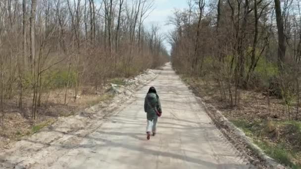 Egy lány sétál a tavaszi erdőben. A helikopter hátulról figyeli a lányt.. — Stock videók