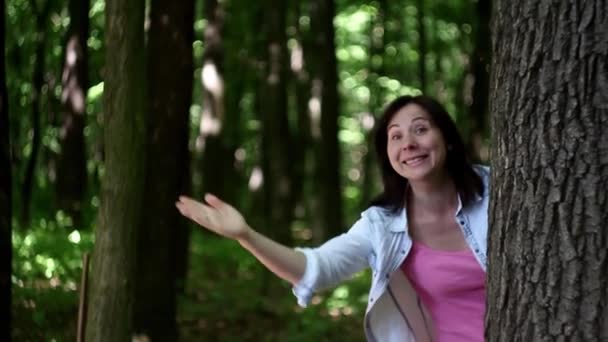 Молода жінка махає з-за дерева в лісі — стокове відео