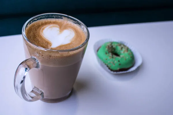 Tasse de café avec un coeur de mousse et beignet — Photo