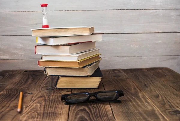 Pile of books and hourglass glasses and pencil — Stock Photo, Image