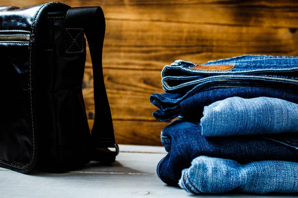 pile of jeans and bag on a wooden background