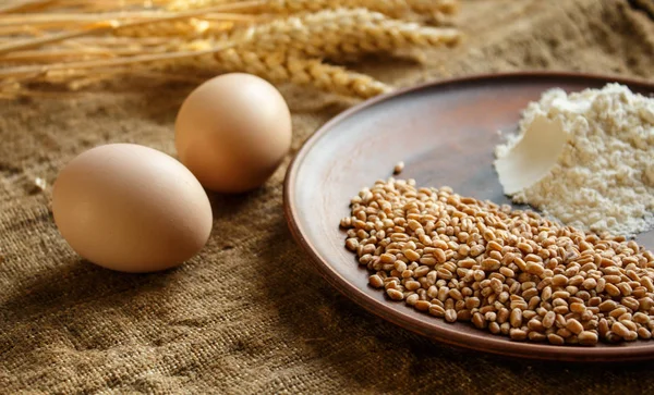 Huevos de harina de trigo y espiguillas de trigo sobre fondo de saco —  Fotos de Stock