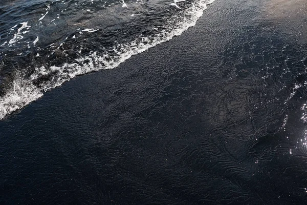 Espuma blanca del océano en la textura volcánica de arena negra — Foto de Stock