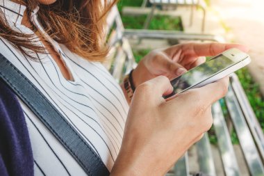 Medya, parkta bir bankta otururken izlemek için onun smartphone kullanarak eller genç kadın. Online alışveriş kavramı